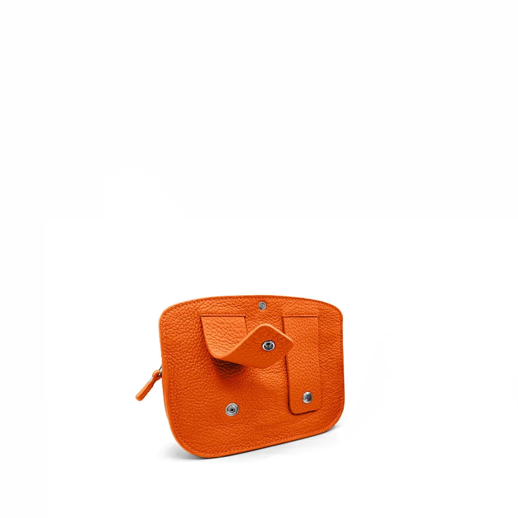 La POCHETTE MAE en cuir orange présente un design de rabat géométrique distinctif et des accents de boutons argentés, sur un fond blanc uni.